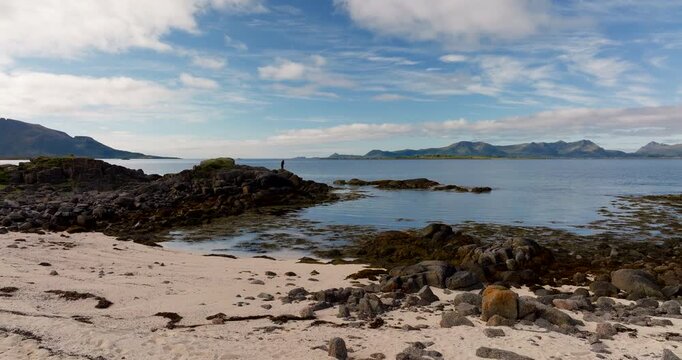 Aerial footage from Aarnessan near Stokmarknes, Norway, reveals a serene arctic coastline with rocky shores, sandy beach, and distant mountain views across the Norwegian Sea