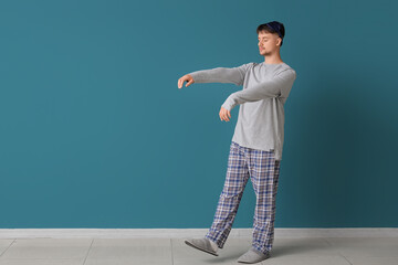 Male sleepwalker in pajamas near blue wall