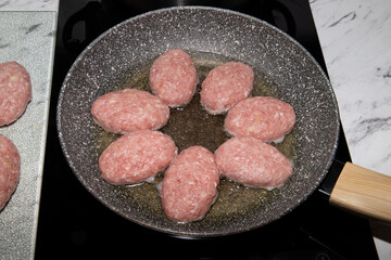 Freshly prepared meat patties. Beef and pork patties are lined up in the kitchen and fried in a pan on the stove. The patty-making process.