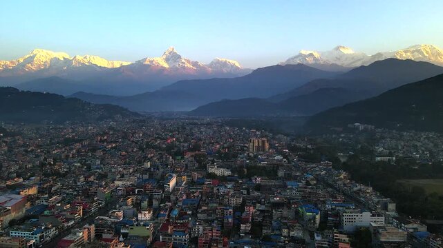 Aerial view of Pokhara city at sunrise with golden light illuminating the Annapurna range and Machhapuchhre peaks, showing the valley&rsquo;s urban landscape framed by majestic Himalayas.