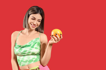 Beautiful young woman with grapefruit on red background