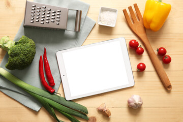 Digital recipe book with napkin, kitchen utensils and ingredients on wooden background