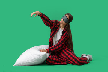 Female sleepwalker in pajamas with pillow sitting on green background