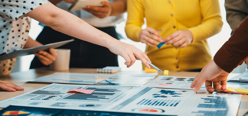 A diverse group of professionals engages in a collaborative meeting, analyzing business charts and graphs, discussing strategies and planning projects in a modern office setting. SACTR