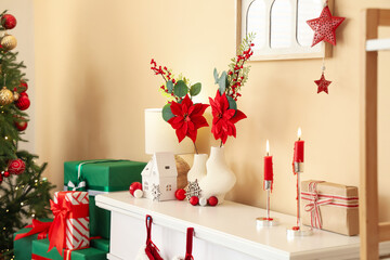 Vase with Christmas flower poinsettia and burning candles on fireplace in living room
