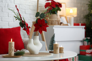 Vase with Christmas flower poinsettia and burning candles on table in living room