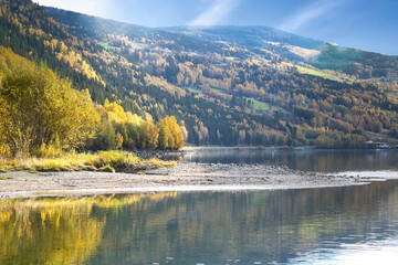 Autumn landscape with colorful forest on the lake shore and mountain backdrop.