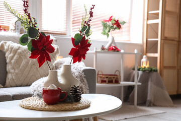 Vase with Christmas flower poinsettia and cocoa on table in living room