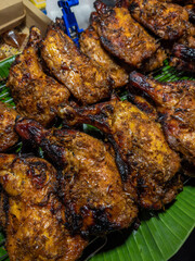 Delicious, golden-brown Filipino Chicken Inasal, grilled to perfection with savory spices and charred skin, displayed appetizingly on a banana leaf at a vibrant street food market.