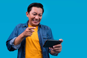 Middle-age Asian Man Points Excitedly at Phone Screen Isolated Against Blue Background