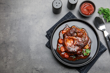 Tasty beef ossobuco with carrot, parsley and sauce served on grey textured table, flat lay. Space for text