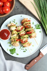 Tasty skewers with chicken, vegetables, sauce and green onion on grey table, flat lay