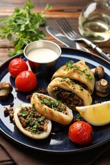 Pieces of tasty grilled squid stuffed with mushrooms, parsley, tomatoes, lemon and sauce on wooden table, closeup