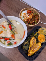 A vibrant spread of authentic Thai dishes featuring creamy Tom Kha Gai, flavorful Pad Kra Pao with a fried egg, and delicious grilled chicken skewers with dipping sauces. A perfect exotic meal.