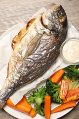 Tasty grilled fish, vegetables and sauce on wooden table, top view