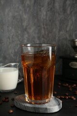 Tasty iced coffee, milk, grinder and beans on black wooden table