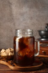 Tasty iced coffee, sugar, grinder and beans on wooden table