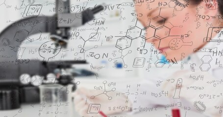 Scientist in lab coat noting with red pen at microscope in research lab, with formulas panel