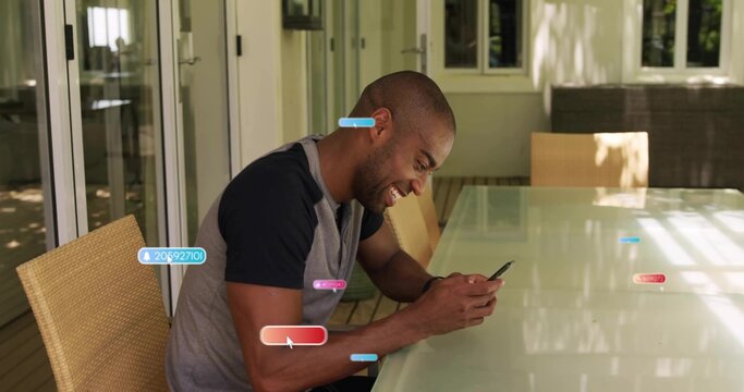 Smiling middle aged man tapping smartphone on glass top table at covered patio, with wicker chairs