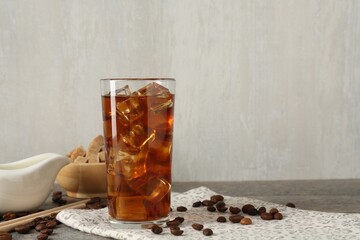 Tasty coffee with ice in glass, beans and sugar cubes on wooden table against grey background, closeup. Space for text