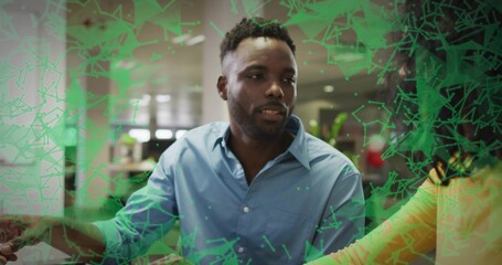 Interacting man in blue shirt studying holographic interface at office table, with seated colleague