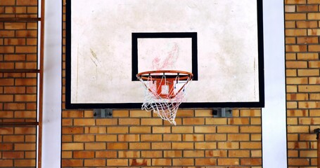 Displaying basketball backboard and rim hanging on brick wall in gym, with net and ladder