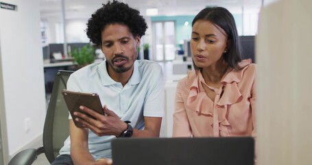 Collaborating coworkers reviewing laptop and tablet at open-plan office, with polo and blouse