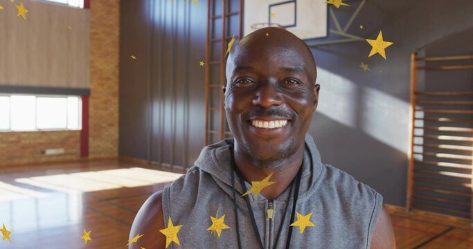 Smiling coach wearing gray sleeveless hoodie and whistle standing on school gym, with lens flares - Powered by Adobe