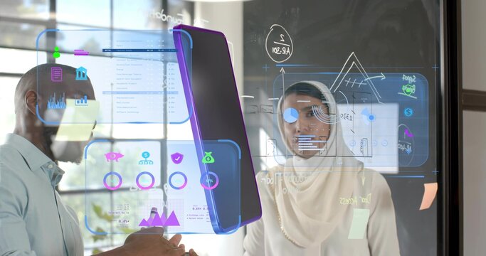 Professionals wearing hijab collaborating in office, with glass panel displaying holographic charts - Powered by Adobe