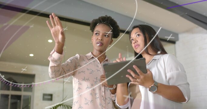 Discussing digital interface by women in business attire in office lobby, with tablet and plant - Powered by Adobe