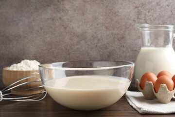 Liquid dough in bowl, whisk and ingredients on wooden table, closeup