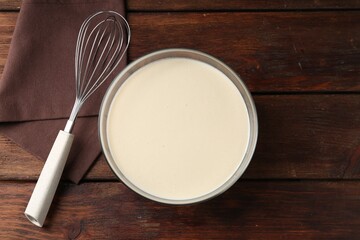 Liquid dough in bowl and whisk on wooden table, top view