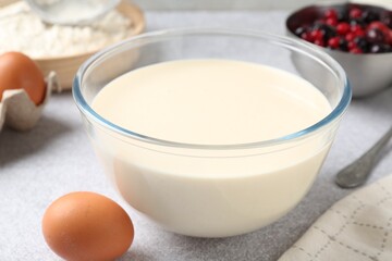 Liquid dough in bowl, berries and ingredients on light grey table, closeup
