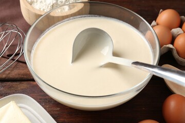 Liquid dough in bowl and ingredients on wooden table, closeup