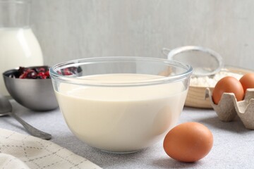Liquid dough in bowl, berries and ingredients on light grey table, closeup