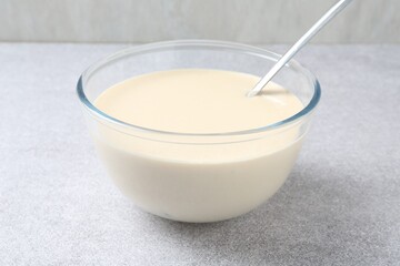 Liquid dough in bowl and ladle on light grey table, closeup