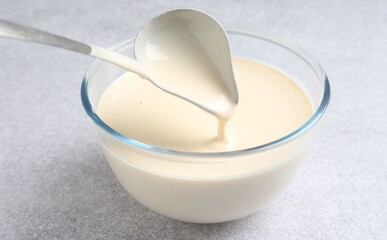 Taking liquid dough from bowl with ladle on light grey table, closeup