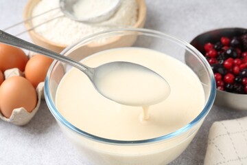Taking liquid dough from bowl with spoon on light grey table, closeup