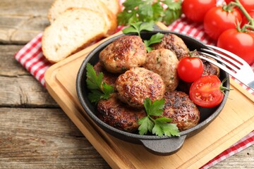 Delicious patties with parsley, tomatoes in pan and fork on wooden table, closeup