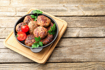 Delicious patties with parsley and tomatoes in pan on wooden table. Space for text