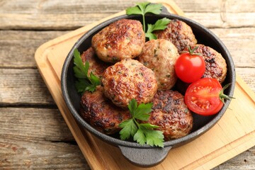Delicious patties with parsley and tomatoes in pan on wooden table, closeup