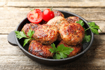 Delicious patties with parsley and tomatoes in pan on wooden table, closeup