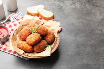 Delicious patties with rosemary in bowl, bread and ketchup on grey textured table. Space for text