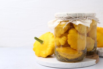 Pickled pattypan squashes in jars and fresh vegetables on white table, closeup. Space for text