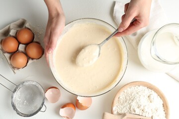 Woman making batter (liquid dough) at white table, top view