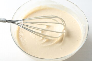 Bowl and whisk with batter (liquid dough) on white table, closeup