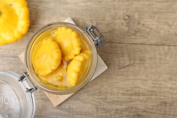 Pickled pattypan squashes in glass jar on wooden table, top view. Space for text