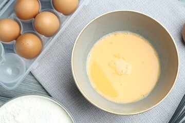 Beaten eggs in bowl and flour on table, flat lay