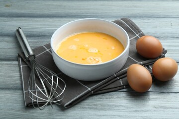 Beaten eggs in bowl and whisk on wooden table, closeup