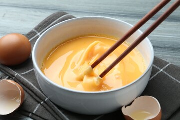 Beaten eggs in bowl and chopsticks on table, closeup